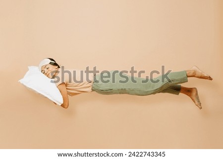 Full body sideways young calm Latin woman wears pyjamas jam sleep eye mask rest relax at home fly fall hover over air on pillow isolated on plain pastel beige background. Good mood night nap concept Royalty-Free Stock Photo #2422743345