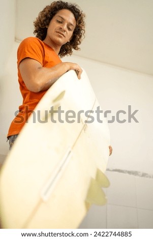 Vertical low angle view photo of a repairman moving a surfboard inside a workshop