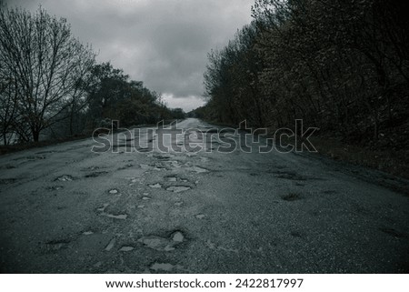 Old gloomy road near trees. Bad asphalt. Gloomy atmosphere. Evening.