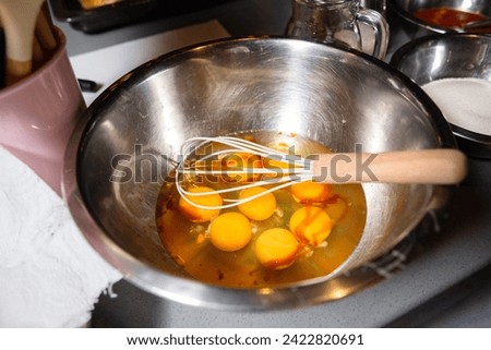 Preparing a meal by whisking fresh eggs in a stainless steel mixing bowl with a wire whisk, with kitchen equipment in the background.
 Royalty-Free Stock Photo #2422820691