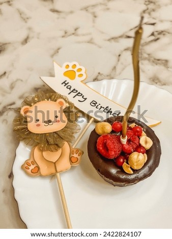 A small brownie chocolate cake on a plate with a golden candle and an axe with the inscription happy birthday, a cardboard lion.
