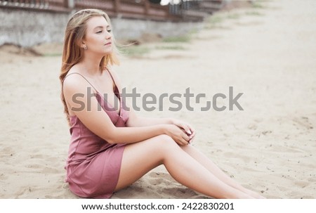 Young woman in pink dress sitting on sand and enjoys sea.