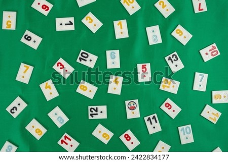 Plastic tiles from the game rummikub, rummy or  okey in Turkey , scattered and arranged on  green background 
