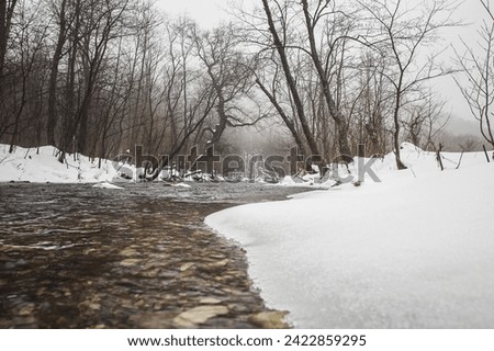 A stunning winter river winds its way through a peaceful forest, framed by snow-covered trees and banks. This serene and picturesque scene is ideal for use in stock photography.