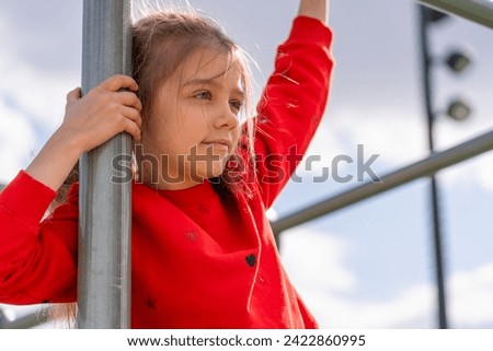 Thoughtful girl wearing crimson red sweater leans gracefully against polished metal pole, merging energy of the city with her own tranquil spirit