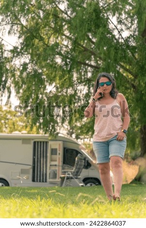 View of a woman talking on the phone walking and a caravan parked in a forest in the background on a vacation adventure trip. copy space available area