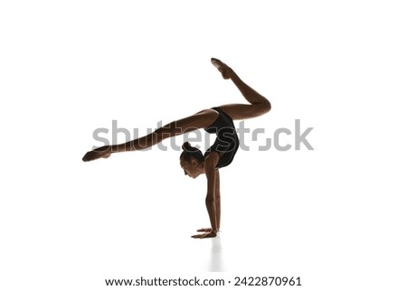 Flexibility and grace. Beautiful teen girl, rhythmic gymnast in black costume performing against white studio background. Concept of sport, beauty and grace, competition, art, youth, hobby