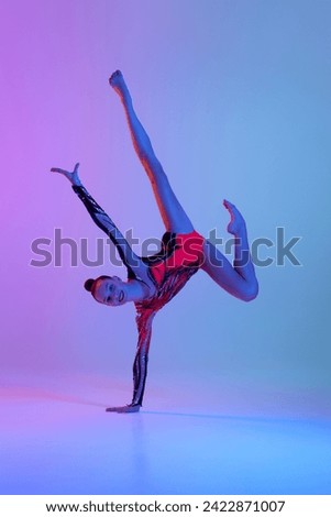 Smiling beautiful teen girl in bright stage costume, rhythmic gymnast dancing against gradient studio background in neon light. Concept of sport, beauty and grace, competition, art, youth, hobby