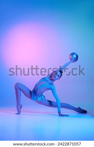 Beautiful teen girl, rhythmic gymnast in sparkling costume training with ball against gradient studio background in neon light. Concept of sport, beauty and grace, competition, art, youth, hobby