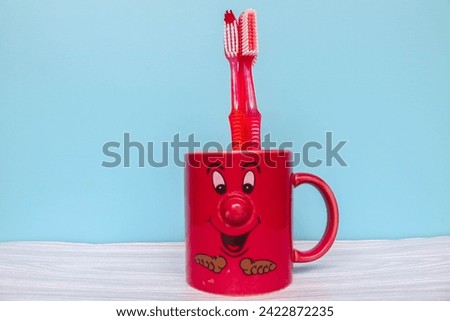 Red toothbrush in red mug cartoon face with copyspace isolated on blue background. Wallpaper red mug and toothbrush on gray table and blue background