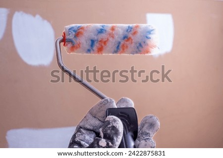 A painter with a black glove holds a small roller with short hair, applying primer to a previously prepared surface and fixed with plaster.