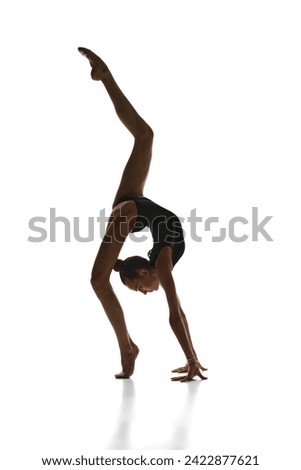 Elegance in movements. Beautiful teen girl, rhythmic gymnast in black stage costume dancing, performing against white studio background. Concept of sport, beauty, grace, competition, art, youth, hobby