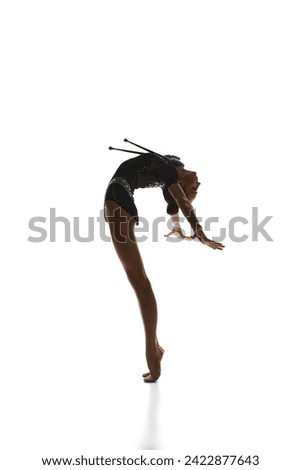 Elegance in movements. Beautiful teen girl, rhythmic gymnast in black stage costume dancing, performing against white studio background. Concept of sport, beauty, grace, competition, art, youth, hobby