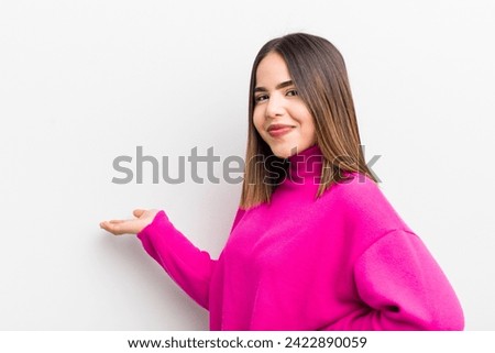 pretty hispanic woman feeling happy and cheerful, smiling and welcoming you, inviting you in with a friendly gesture
