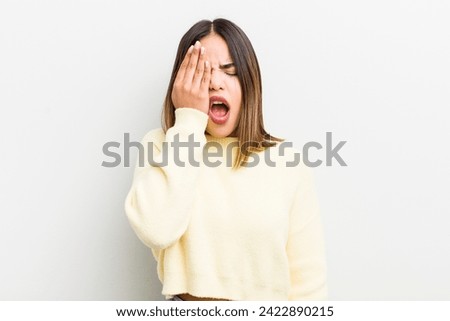 pretty hispanic woman looking sleepy, bored and yawning, with a headache and one hand covering half the face