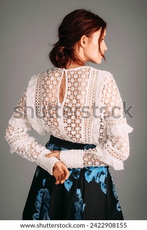 Embroidery long sleeve blouse in white, rear view. Studio portrait of young beautiful ginger lady. Natural makeup and hairdo with red lips. Evening outfit,  female fashion. Transparent elegant dress. Royalty-Free Stock Photo #2422908155