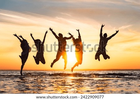 Group of happy young friends are having fun and jumping at calm sunset beach Royalty-Free Stock Photo #2422909077
