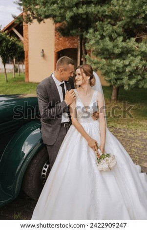 A handsome groom embraces his bride in a lush white dress and smiles in a beautiful outdoor setting. Under the open sky. High quality photo. A newlywed couple poses together on a sunny summer day.