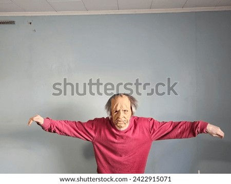 A person wearing a creepy mask standing by a bare wall with their arms out.