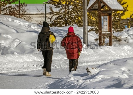 Mother and daughter walk along a snow-covered sidewalk on a winter day