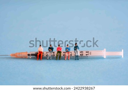 miniature figures of people sitting on a medical syringe