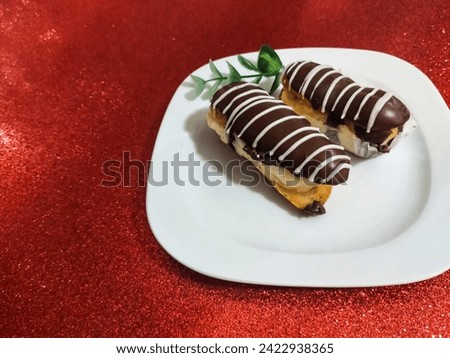 Chocolate eclairs in a white square dish on a red glitter background Royalty-Free Stock Photo #2422938365