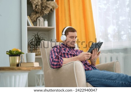 With headphones for immersion, he uses a tablet for entertainment or work, a common sight in today's tech-savvy society. Royalty-Free Stock Photo #2422940047