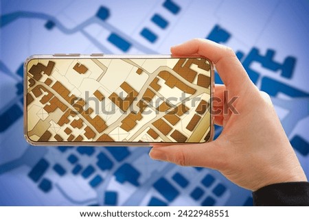 Hand holding a smartphone with an imaginary cadastral map of territory with buildings and land parcels - land registry and digital services concept image. 