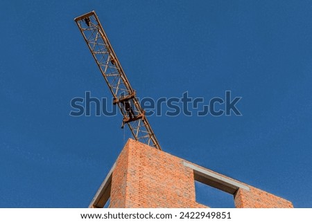 It's view of incomplete red brick house without roof. It is close up view of unfinished apartment building. Its sunny day. It's a photo of a tower crane.