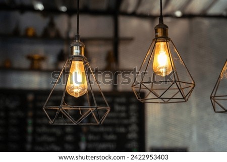 Classic style lightbulb ceiling lamp with iron cage glowing in orange light shade. Interior decoration object photo, selective focus.
