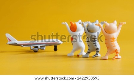 Three toy kittens with raised legs and passenger airplane on yellow background. Concept of greeting the arriving airplane flight and air passengers. Toy world. Photo. Selective focus. Close-up