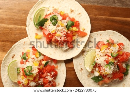 Delicious tacos with vegetables and lime on wooden table, top view