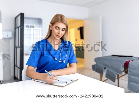 Portrait of young female doctor sitting in clinic office, filling out medical form at table.