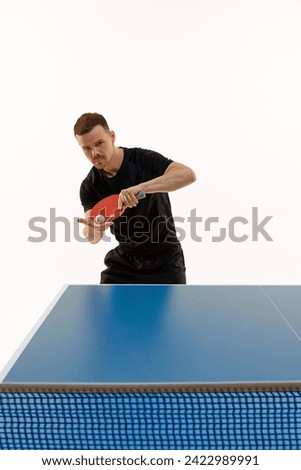 Man in black sport uniform playing table tennis, focused on ball to make perfect serve against white background. Concept of professional sport, championship, tournament, victory and winner. Ad