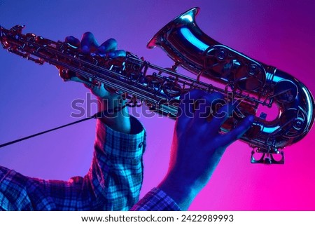 Cropped portrait of jazzman playing saxophone against gradient blue-pink background in neon light. Jazz melodies. Concept of classical musical instrument, concerts and festivals. Ad
