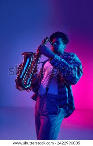 Jazz musician in retro outfit virtuously playing saxophone against gradient blue-pink background in neon light. Concept of blues, classy instrumental music, festivals and concerts. Ad