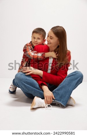 Family portrait of beautiful young mother embracing with little boy, son against white background. Kid showing support and care. Concept of happiness, Mother's day, childhood, fashion and lifestyle