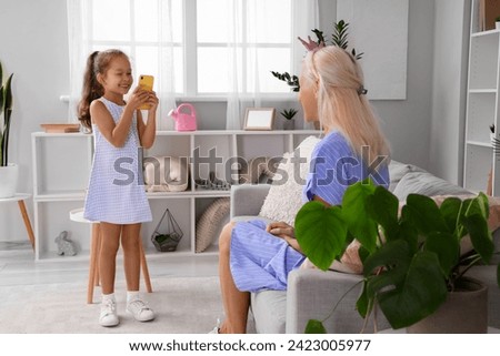 Little girl taking picture of her grandmother with crown at home