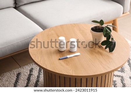 Pregnancy test with pill bottles and plant on table in living room Royalty-Free Stock Photo #2423011915