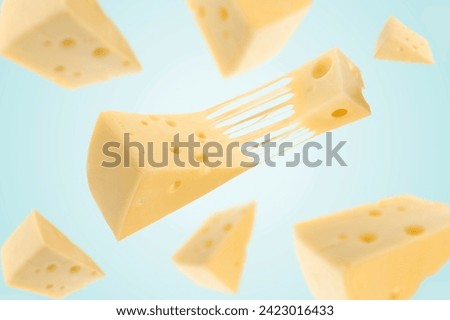 Pieces of cheese falling on light blue background Royalty-Free Stock Photo #2423016433