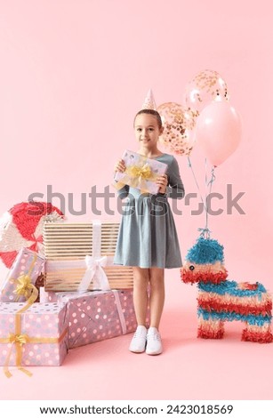 Cute little girl in party hat with Birthday gifts on pink background