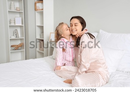 Little girl kissing her happy mom in bedroom. Mother's Day celebration