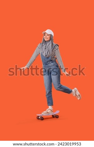 Young Muslim woman in hijab skating on orange background