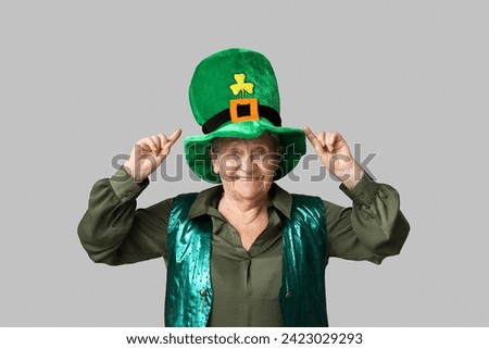 Senior woman pointing at leprechaun hat on grey background. St. Patrick's Day celebration