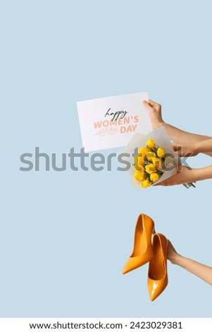 Female hands with bouquet of tulips, high heel shoes and festive postcard on blue background. International Women's Day celebration