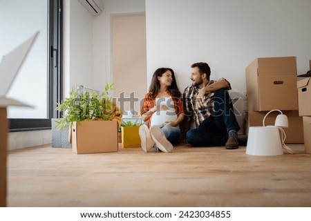 Beautiful young couple expecting a baby just moved into an empty apartment, sitting among cardboard boxes making plans for future. New beginnings