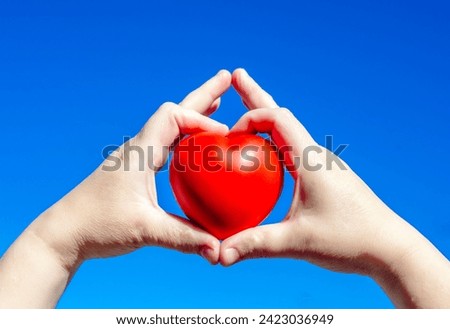 Girl holding a heart on a background against the blue sky
