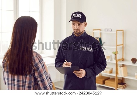 Police officer interrogating witness, victim or suspect. Serious policeman who is working on felony, burglary, or fraud case, asks young woman questions and takes notes. Crime investigation concept Royalty-Free Stock Photo #2423045129