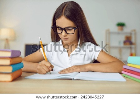 Portrait of clever school child. Little student girl in glasses sitting at desk, studying new things and writing in notebook. Learning and education concept Royalty-Free Stock Photo #2423045227