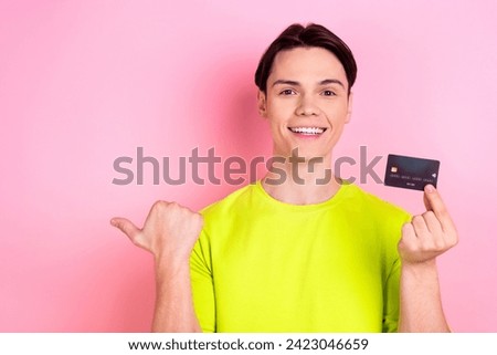Photo portrait of pretty teen man hold credit card point empty space wear trendy yellow clothes isolated on pink color background